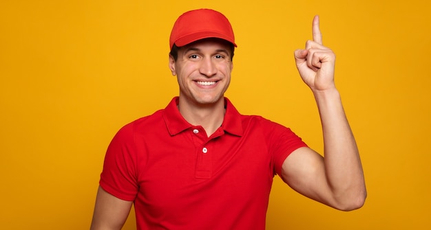 Handsome young happy courier or delivery man in red uniform is posing isolated on yellow background