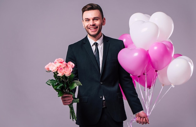 Handsome young happy man holds the bouquet of roses and balloons. Celebration, holidays and gifts concepts. St Valentines dat. Lovers day