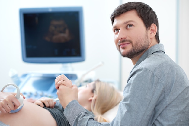 Photo handsome young  husband carrying about his pregnant wife who diagnosing at ultrasound, screening stomach at hospital.