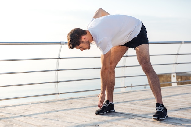 Handsome young male athlete doing morning exercises on wooden terrace