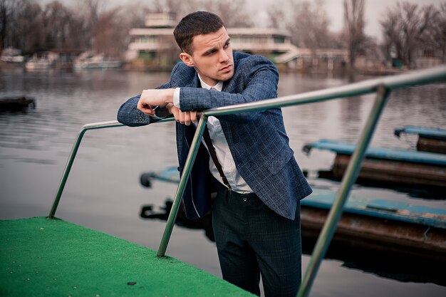 Красивый молодой мужской бизнесмен стоит на скамье подсудимых на лодочной станции
