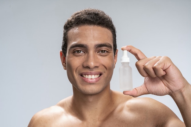 Handsome young male smiling holding a bottle of cosmetics