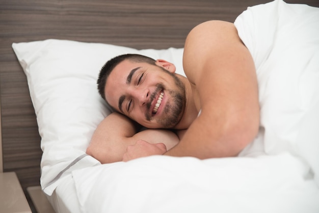 Красивый молодой студент мужского пола счастливо спит в белой постели