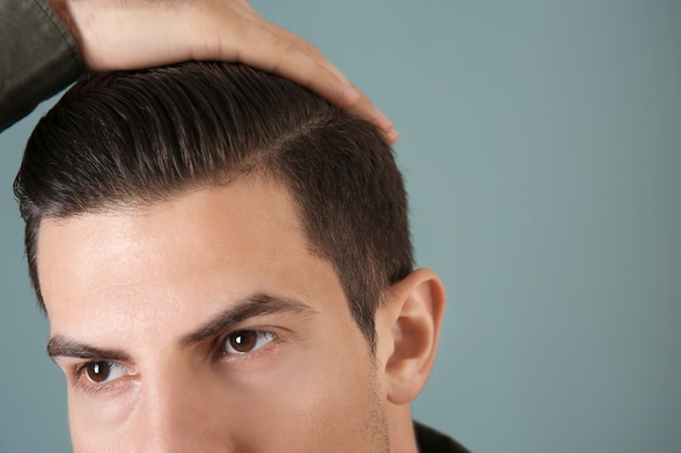 Handsome young man applying clay for hair on grey