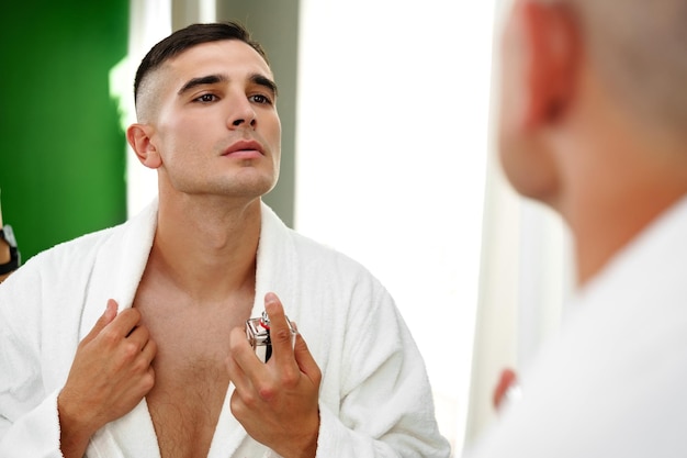 Photo handsome young man applying perfume in the bathroom