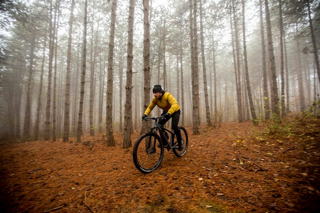 Bel giovane in bicicletta attraverso la foresta di autunno