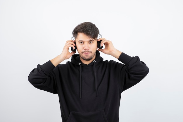 Handsome young man in black hoodie wearing big wireless music headphones 