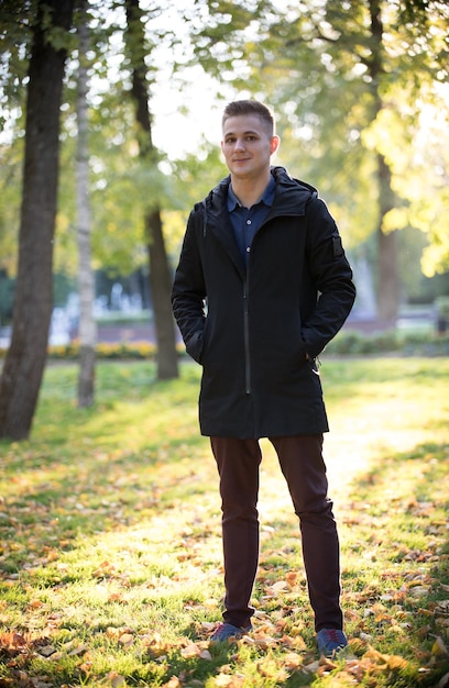 Photo handsome and young man in a black jacket standing in the park