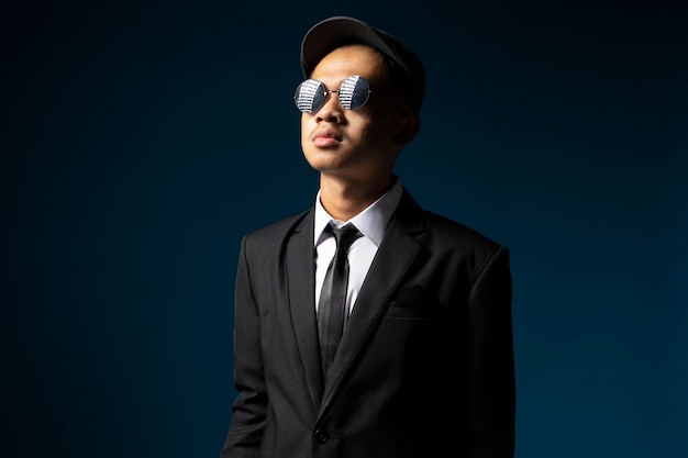 Photo handsome young man in black suit wearing hat and glasses facing dark themed light