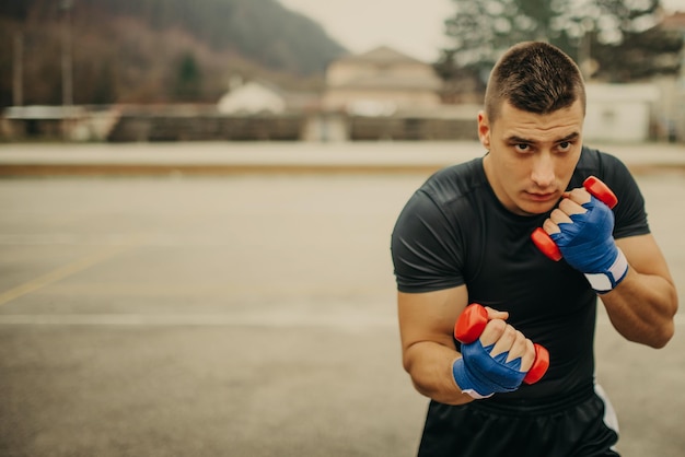 Handsome young man boxer practicing shadow boxing with dumbbells