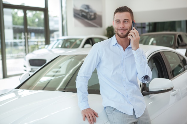 Handsome young man buying a new car at dealership salon