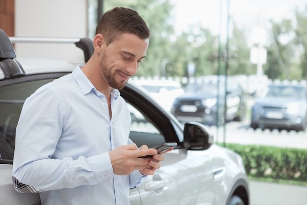 Handsome young man buying a new car at dealership salon