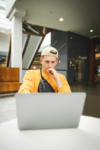 Handsome young man in a cap and a yellow lily works with a computer