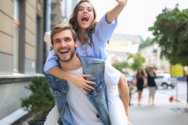 Handsome young man carrying young attractive woman on shoulders while spending time together outdoors.