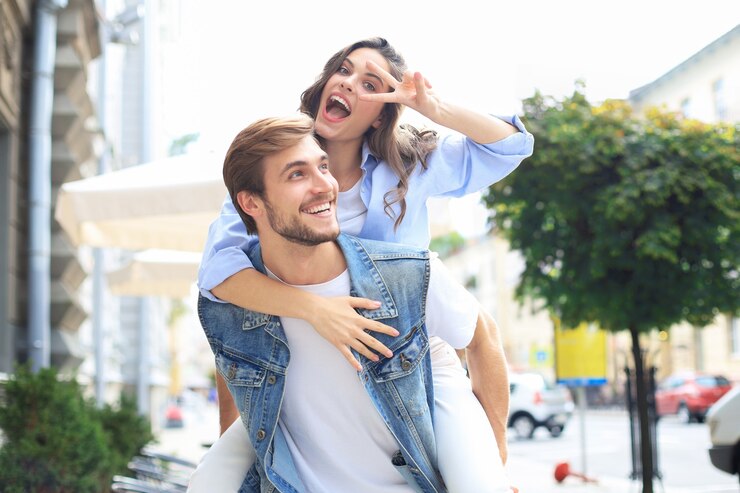 Photo handsome young man carrying young attractive woman on shoulders while spending time together outdoors.
