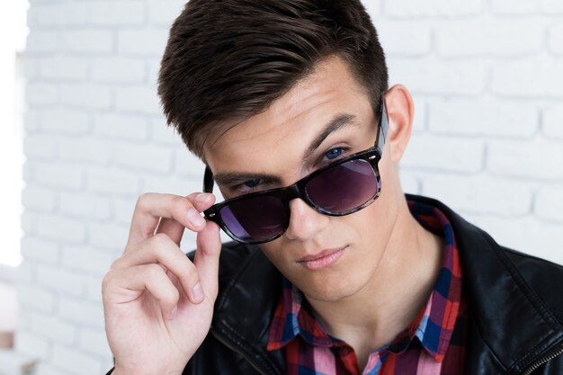 Handsome young man in casual clothes, standing against white brick wall