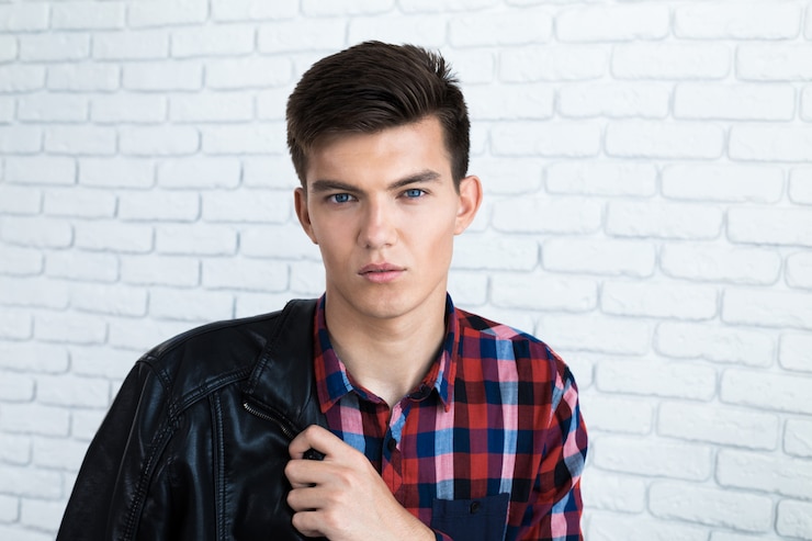 Photo handsome young man in casual clothes, standing against white brick wall
