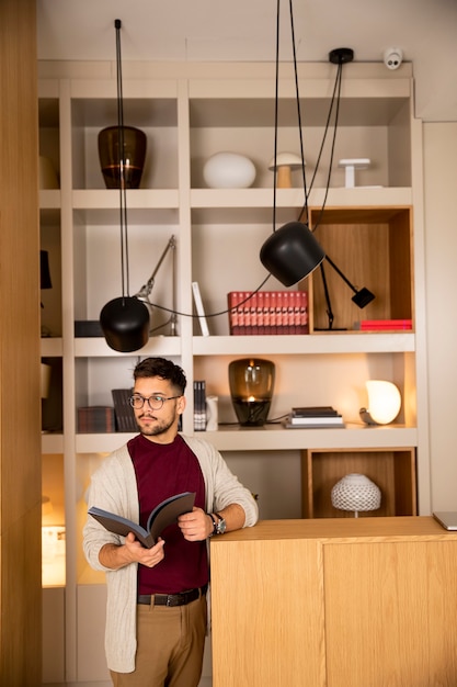 Handsome young man in casual clothes and with eyeglasses reading a book at home