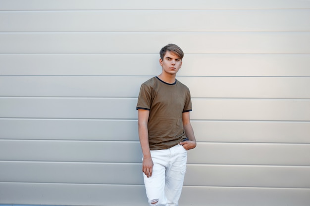 Handsome young man in a classic fashion T-shirt and white pants near a modern wall