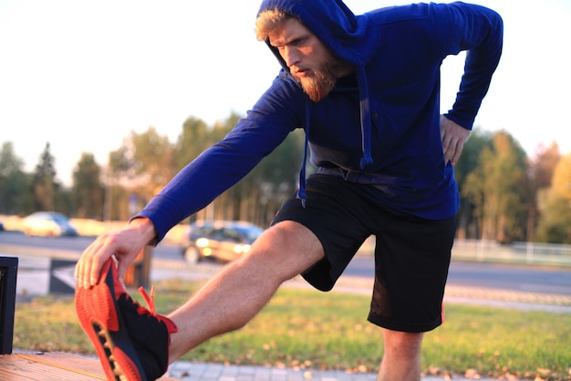 Handsome young man doing stretching exercises before running while standing outdoors