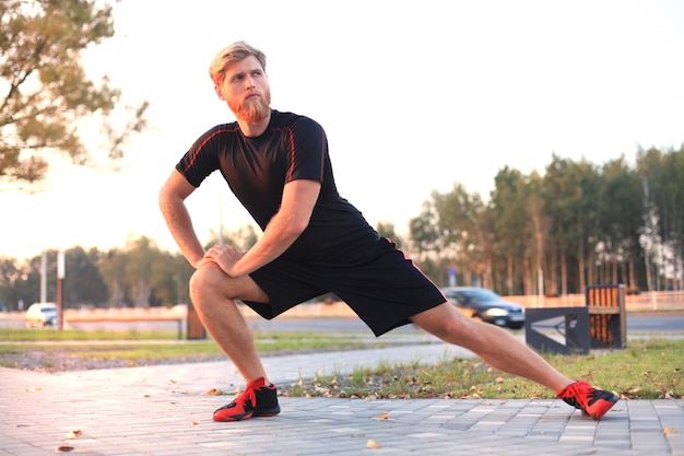 Handsome young man doing stretching exercises before running while standing outdoors