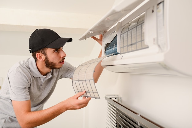 Handsome young man electrician cleaning air filter on an indoor unit of air conditioning system in a client house