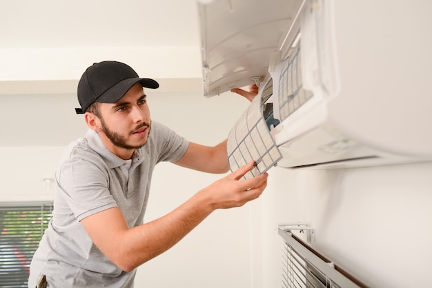 Handsome young man electrician cleaning air filter on an indoor unit of air conditioning system in a client house