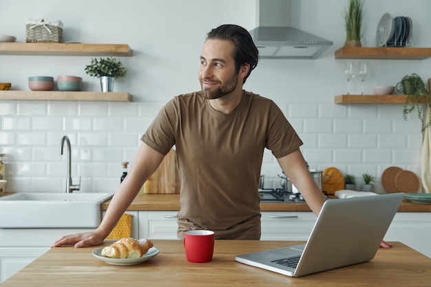 キッチンで時間を過ごす間朝食を楽しみ思慮深く見えるハンサムな若い男性