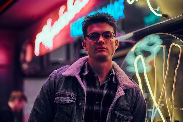 A handsome young man fashionably dressed standing in the street at night. Illuminated signboards, neon, lights.