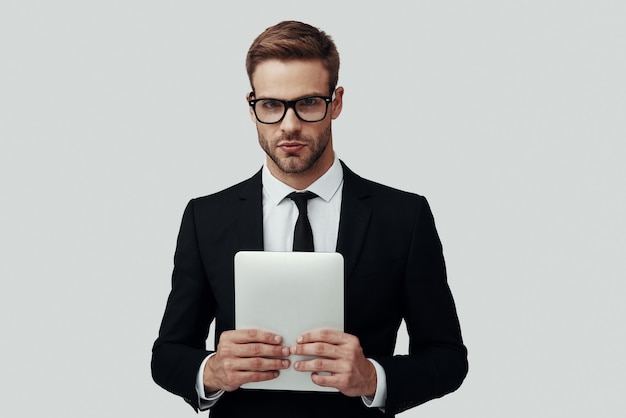 Handsome young man in formalwear looking at camera while standing against grey background