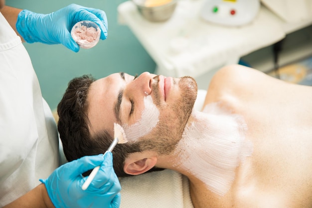 Handsome young man getting a facial treatment and an anti-aging mask in a health spa