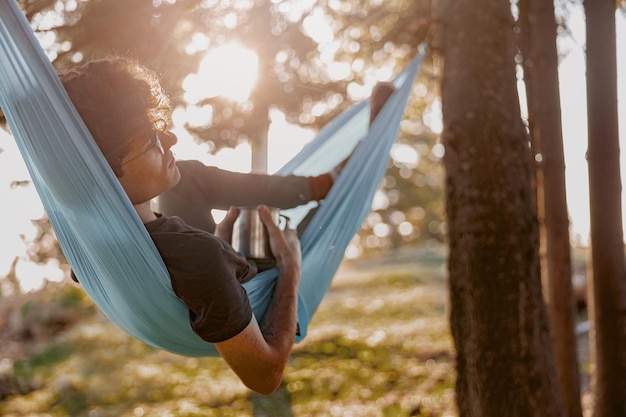 Photo handsome young man in glasses lying in hammock and relaxing with coffee forest travel