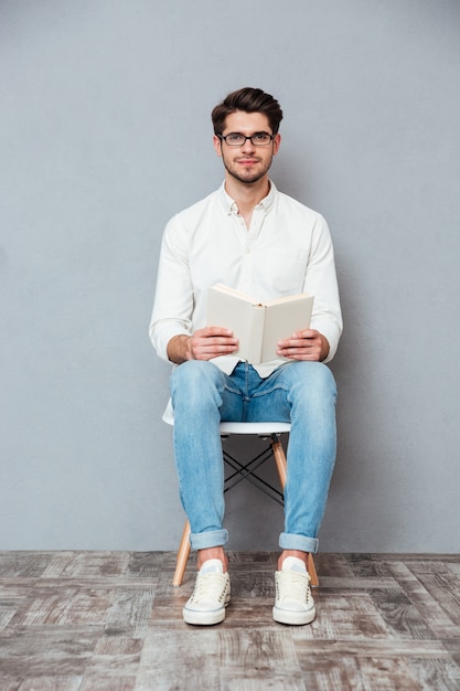 Handsome young man in glasses sitting on chair and reading a book