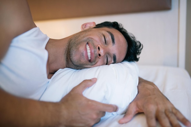 Красивый молодой человек счастливо и улыбается на фоне белой кровати Спальня