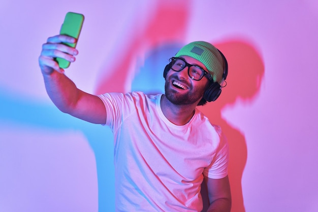 スマートフォンでセルフィーを撮って笑っているヘッドフォンをかぶったハンサムな若い男性