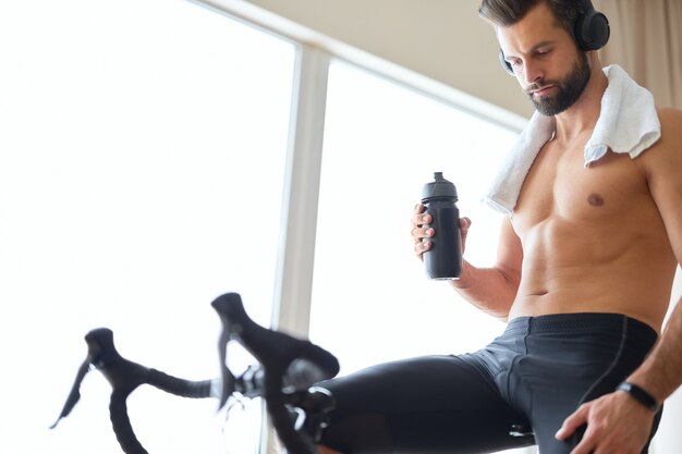 Handsome young man in headphones using bicycle trainer at home