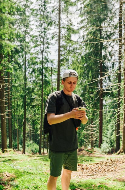 Handsome young man hiker in casual clothes uses a smartphone in a thick coniferous forest vertical