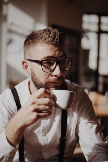 handsome young man holding coffee while sitting in cafe