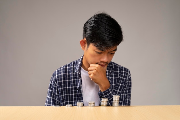 Handsome young man holding a hand chin dream plan thinking how to save with coins in front of him