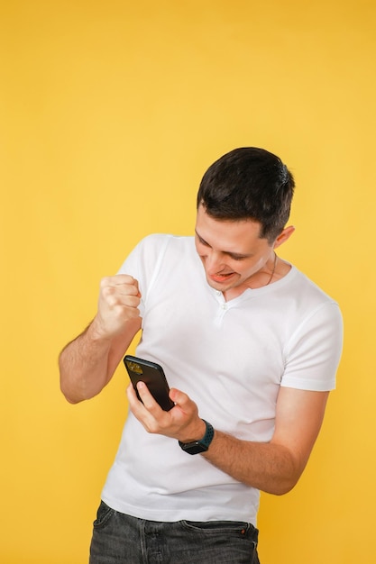 Foto giovane bello che tiene un telefono in mano che parla emotivamente al telefono su uno sfondo giallo semplice