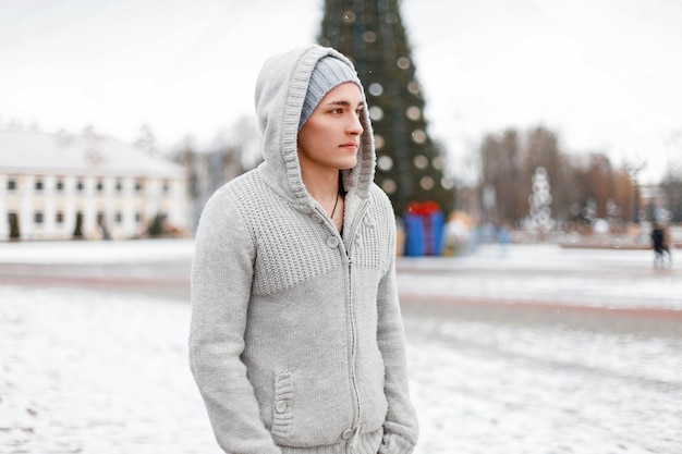 Handsome young man in a hood in a knitted sweater and hat in winter day