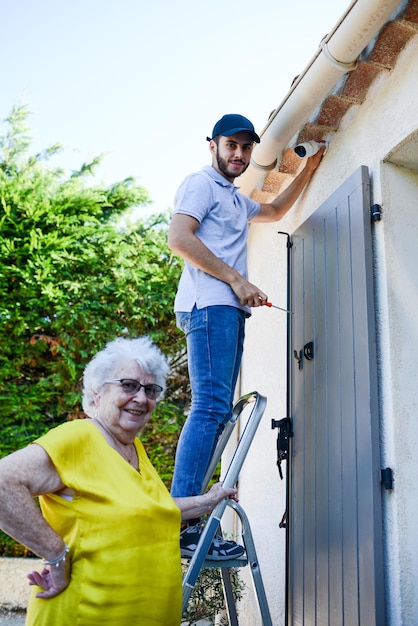 Handsome young man installing house security anti burglary camera and siren alarm in a senior woman home