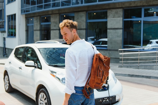 ハンサムな若い男が彼の現代の電気自動車を充電しています。