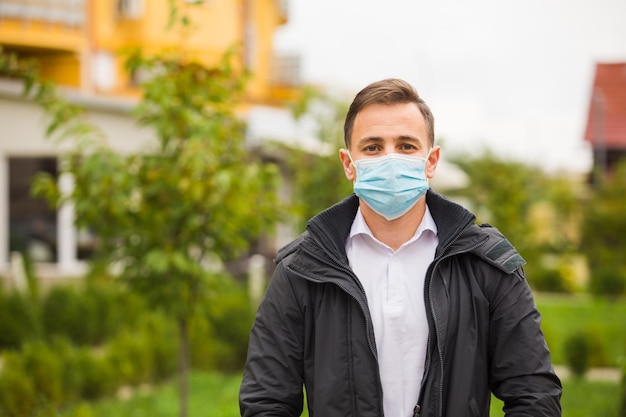 Il bel giovane è in piedi all'aperto con una maschera protettiva si trova in giardino e guarda la telecamera