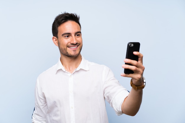 Handsome young man over isolated blue background making a selfie