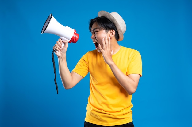 Handsome young man over isolated blue background shouting through a megaphone