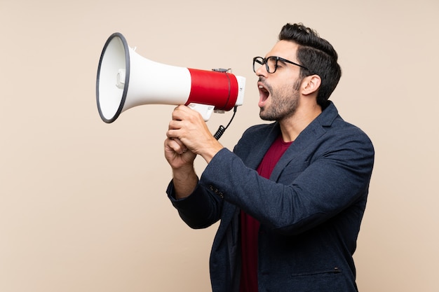 Handsome young man over isolated wall shouting through a megaphone