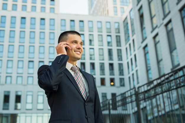 建物の背景に手に携帯電話とジャケットのハンサムな若い男