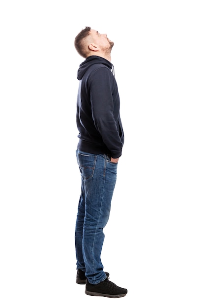 A handsome young man in jeans is standing. Hands in pockets. Side view. Isolated over white . Vertical.