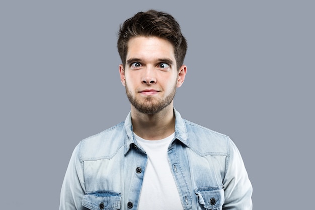 Handsome young man joking and making funny face over gray background.